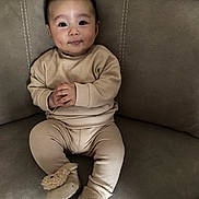Hady is registered to the contest to win money with this photo: baby, infant, child, face, hands, pajamas, slippers, couch, furniture, seated, indoors, cute, smiling, cozy, soft, woolen, expression, looking_at_camera, plush, comfortable