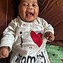 baby, child, smiling, laughing, curly_hair, onesie, clothing, text, heart, love, couch, blanket, indoor, happy, infant, person, face, cute, joy, portrait