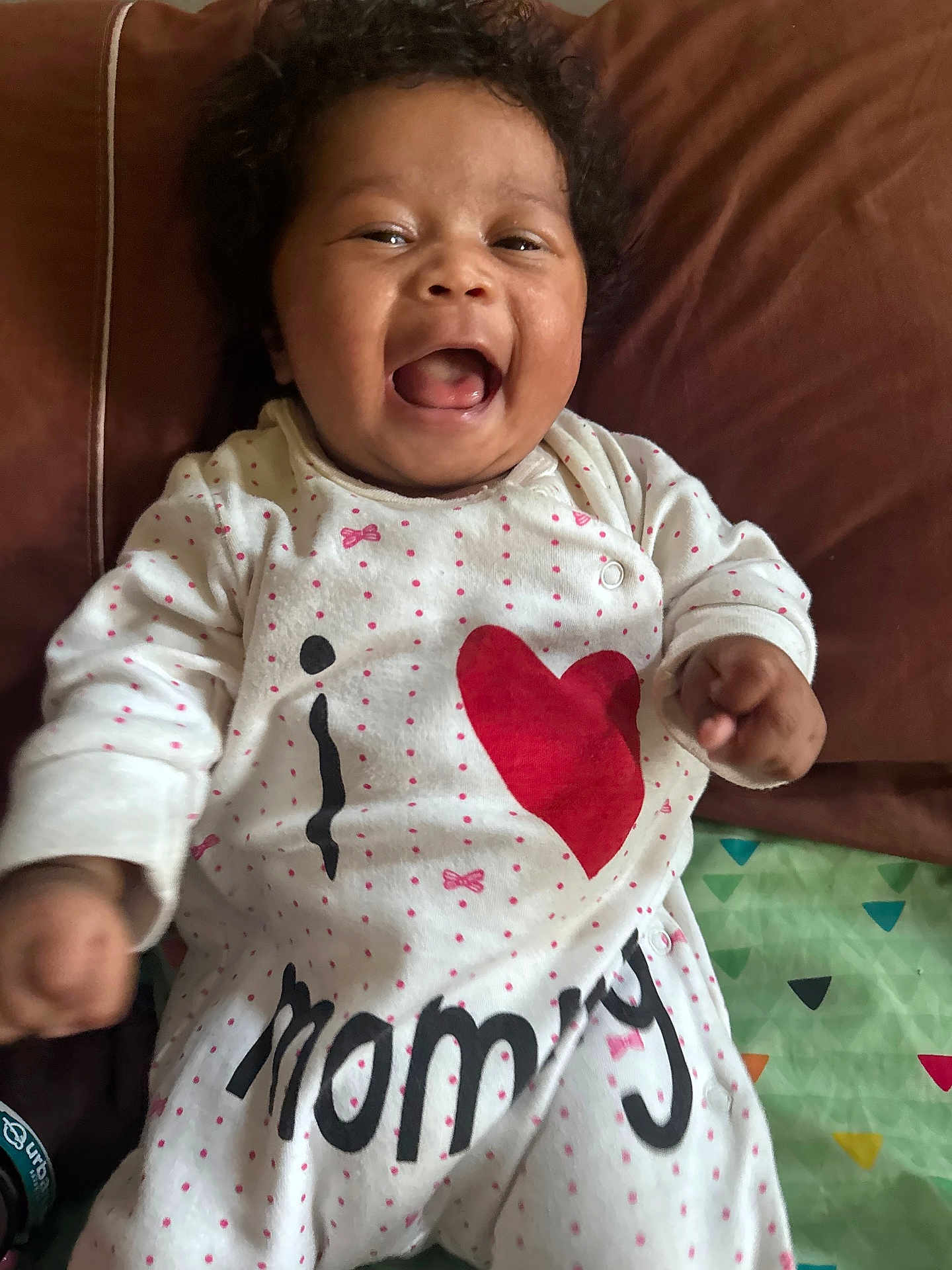 Makayla joined the competition — help win amazing prizes! baby, child, smiling, laughing, curly_hair, onesie, clothing, text, heart, love, couch, blanket, indoor, happy, infant, person, face, cute, joy, portrait