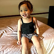 Bri joined the competition — help win amazing prizes! bed, bedspread, black_tank_top, casual_clothing, child, cute, face, furniture, hair, happy, home, indoor, legs, leopard_print_shorts, light, person, sitting, smiling, toddler, young_child