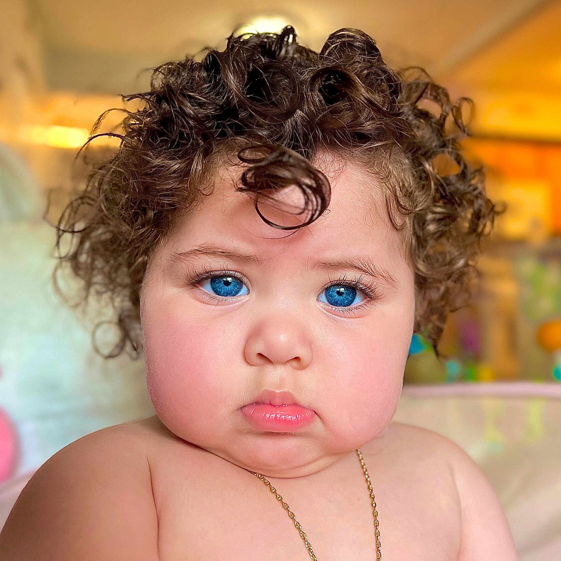 Selena is registered to the contest to win money with this photo: baby, blue_eyes, blurred_background, child, chubby_cheeks, closeup, curly_hair, cute, expression, face, indoor, infant, innocence, necklace, person, portrait, serious, skin, soft_lighting, young_child