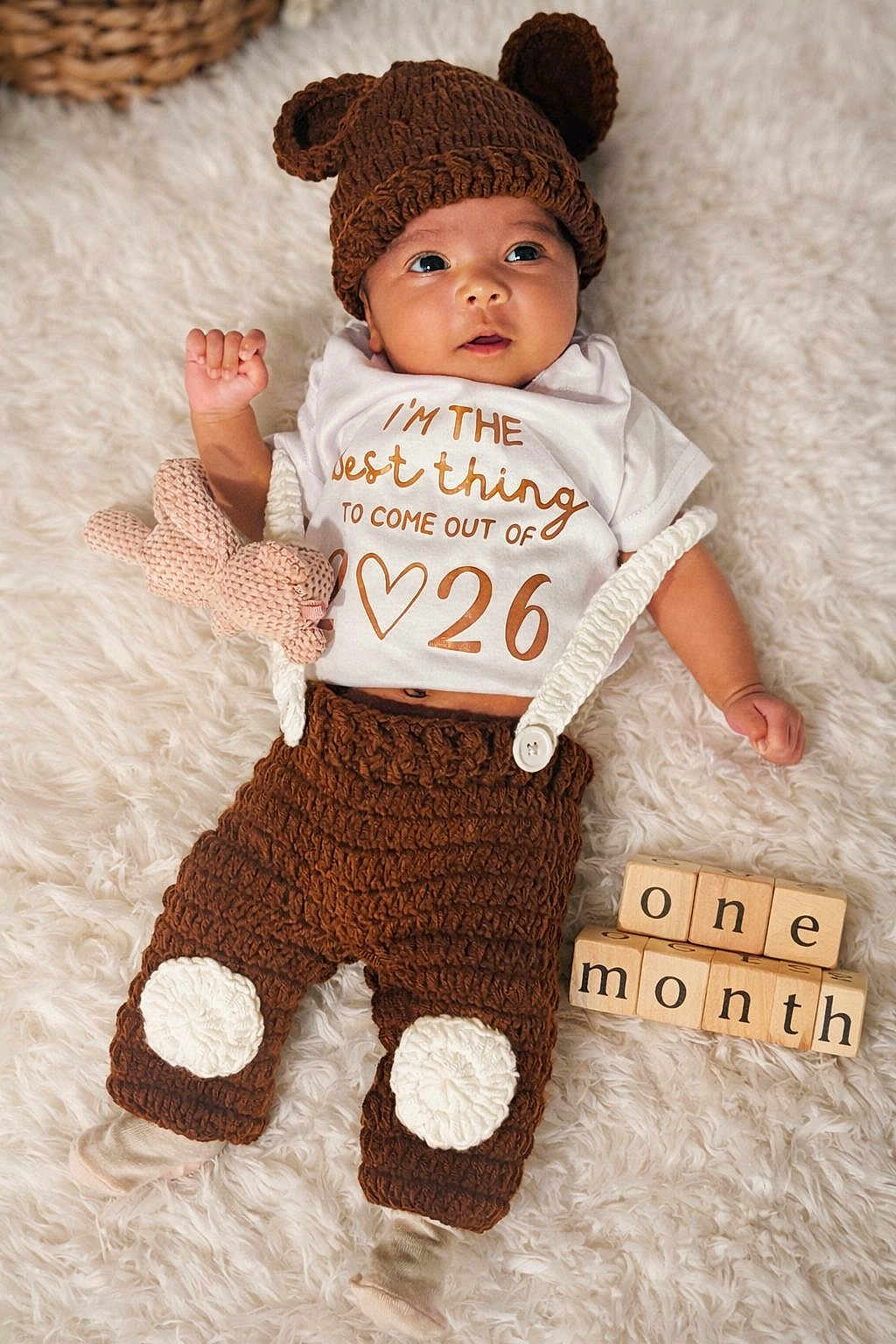 Gianah Fernando is registered to the contest to win money with this photo: baby, infant, newborn, knit_hat, brown_hat, onesie, text_on_shirt, wooden_blocks, blocks, plush_toy, blanket, furry_blanket, crochet_pants, brown_clothing, cute, portrait, milestone, one_month, hands, face