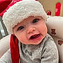 baby, child, santa_hat, red_hat, gray_shirt, teddy_bear_pattern, chair, cute, face, expression, indoors, holiday, festive, smiling, portrait, person, infant, seat, cozy, playful