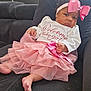 baby, infant, girl, pink_bow, pink_skirt, white_top, couch, indoor, clothing, foot, hand, face, headband, portrait, child, sitting, furniture, expression, cute, home