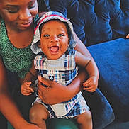 Ahmaj Tigner joined the competition — help win amazing prizes! baby, woman, child, smile, happy, plaid, hat, braids, couch, indoor, person, holding, seated, clothing, home, joy, cute, family, toddler, portrait