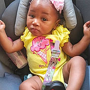 Serenity is registered to the contest to win money with this photo: baby, child, car_seat, headband, flower, yellow_onesie, infant, cute, smiling, skin, seatbelt, baby_toy, pink, indoor, person, portrait, relaxed, small, legs, arms