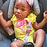 baby, child, car_seat, headband, flower, yellow_onesie, infant, cute, smiling, skin, seatbelt, baby_toy, pink, indoor, person, portrait, relaxed, small, legs, arms