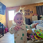 Harper is registered to the contest to win money with this photo: toddler, child, smiling, indoor, playful, onesie, pony_tail, toys, basket, wooden_floor, photographs, curtains, furniture, door, cozy, happy, person, room, home, baby