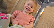 Harper is registered to the contest to win money with this photo: child, toddler, smiling, indoor, playpen, mesh, blanket, pillow, pink_dress, happy, face, person, home, cute, baby, furniture, wood, light, cozy, background