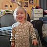 toddler, child, smiling, pajamas, indoor, baby_photos, blanket, chair, curtains, dresser, furniture, happy, home_interior, person, portrait, room, sleepsuit, standing, wooden_wall, young_child