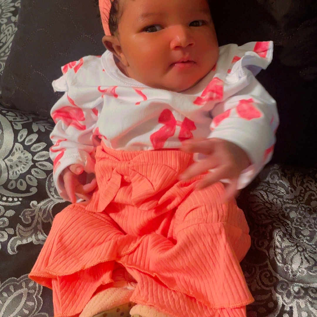 Ryleigh joined the competition — help win amazing prizes! baby, infant, child, headband, coral_clothing, patterned_blanket, smile, cute, portrait, indoors, sitting, hand, face, person, fashion, cozy, young_child, colorful_clothes, soft_texture, blanket