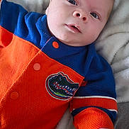 Elijah joined the competition — help win amazing prizes! baby, infant, newborn, onesie, orange_clothing, blue_clothing, blanket, bedding, face, eyes, hand, portrait, close_up, cute, sleepy, gator_patch, sports_logo, fabric, indoor, soft_texture