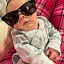 Elijah is registered to the contest to win money with this photo: baby, infant, sunglasses, onesie, blanket, hand, drool, portrait, face, cute, sleepy, indoor, holding, accessory, black_sunglasses, skin, pink, pattern, person, close_up