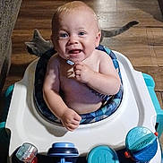 Braxton is registered to the contest to win money with this photo: baby, child, infant, smiling, happy, portrait, high_chair, baby_walker, toy, indoor, wood_floor, cat, pet, seated, blue, white, clothing, home, playtime, closeup