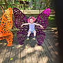 Emerie joined the competition — help win amazing prizes! child, smiling, butterfly_bench, purple, orange, hat, outdoor, wooden_deck, tree, leaves, sunlight, playful, summer_clothing, happy, person, bench, nature, greenery, cute, casual