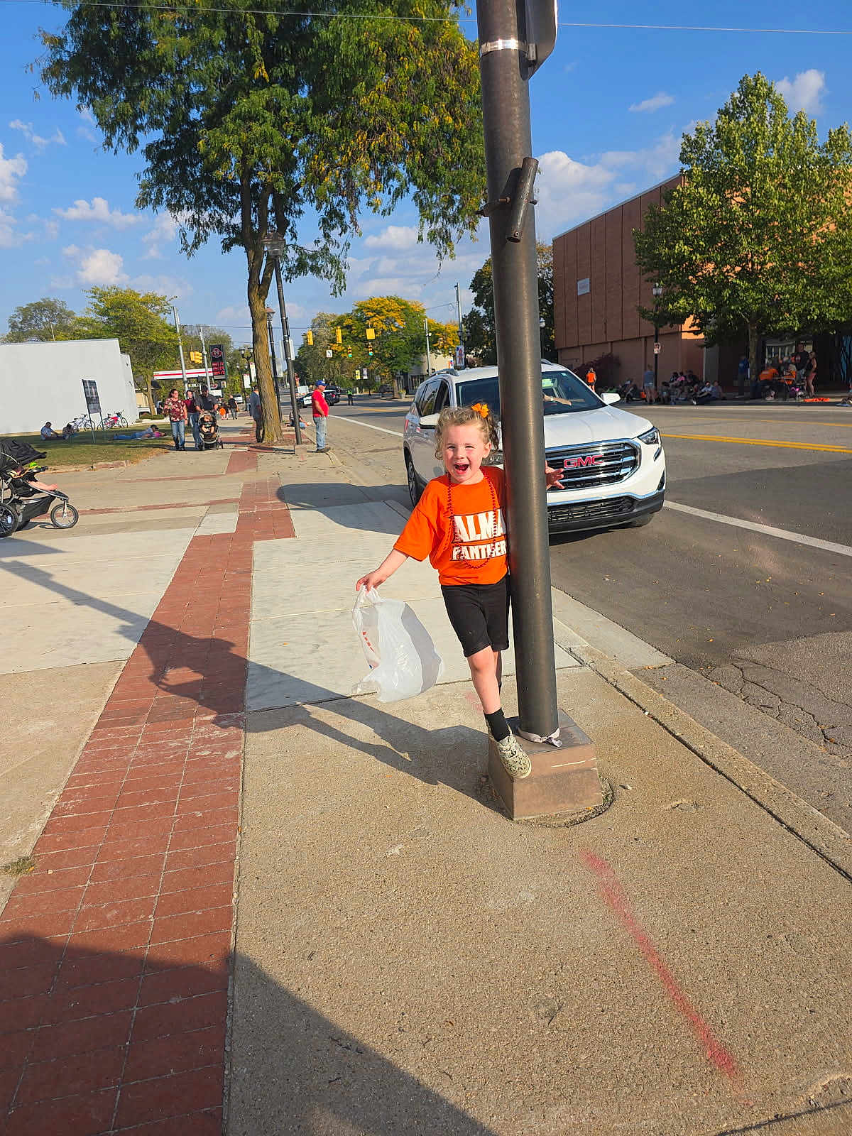 Emerie joined the competition — help win amazing prizes! child, orange_shirt, streetlight, sidewalk, plastic_bag, happy, smiling, urban, daylight, tree, car, road, pedestrian, playful, people, building, traffic_light, shoes, concrete, outdoor