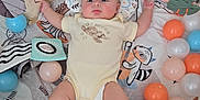 Jack is registered to the contest to win money with this photo: baby, infant, playpen, toy, stuffed_animal, ball, carpet, floor, clothing, onesie, face, child, indoor, cute, colorful, soft_toy, patterned, lying_down, curious, padded