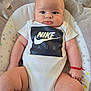 baby, infant, onesie, clothing, nike_air, red_bracelet, baby_seat, cushion, star_pattern, face, skin, arms, legs, indoor, portrait, cute, child, person, comfort, expression