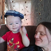 Joshua is registered to the contest to win money with this photo: adult, blue_hat, cartoon_shirt, child, couch, curtains, face, family, floral_pattern, happy, home, indoor, parent, portrait, red_shirt, selfie, sitting, smiling, toddler, woman