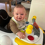 Marius participe au concours pour gagner de l'argent avec cette photo : baby, walker, toy, smile, indoor, child, bib, clothing, floor, wooden_furniture, table, chair, happy, person, play, face, hand, light, household, flooring