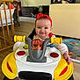 baby, child, walker, red_headband, smile, indoor, floor, toy, yellow, white, person, happy, face, hand, living_room, wood_floor, playtime, cute, infant, furniture