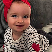 Garence participe au concours pour gagner de l'argent avec cette photo : baby, blanket, child, closeup, clothing, cute, face, hand, happy, headband, heart_patch, indoor, infant, lying_down, person, portrait, red_bow, smiling, striped_shirt, young
