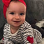 baby, blanket, child, closeup, clothing, cute, face, hand, happy, headband, heart_patch, indoor, infant, lying_down, person, portrait, red_bow, smiling, striped_shirt, young