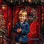 child, boy, denim_jacket, christmas_wreath, red_door, christmas_tree, snow, lantern, holiday, festive, decorations, smile, winter, pine_cones, outdoor, seasonal, happy, portrait, young, celebration