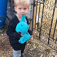 Ethan joined the competition — help win amazing prizes! child, boy, stuffed_animal, blue, toy, outdoor, gate, gravel, plant, black_jacket, sneakers, curious, blond_hair, casual_clothing, fence, daylight, playful, young, cute, portrait