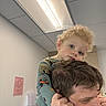 child, toddler, man, piggyback, indoor, pajamas, curly_hair, blue_eyes, smile, ceiling_light, office, wall, person, holding, head, face, casual, closeup, affection, family