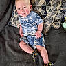 toddler, child, smile, sitting, couch, pillow, patterned_pillow, blue_clothing, shorts, shirt, footwear, colorful_shoes, indoor, happy, rosy_cheeks, baby, person, portrait, cute, casual_clothing