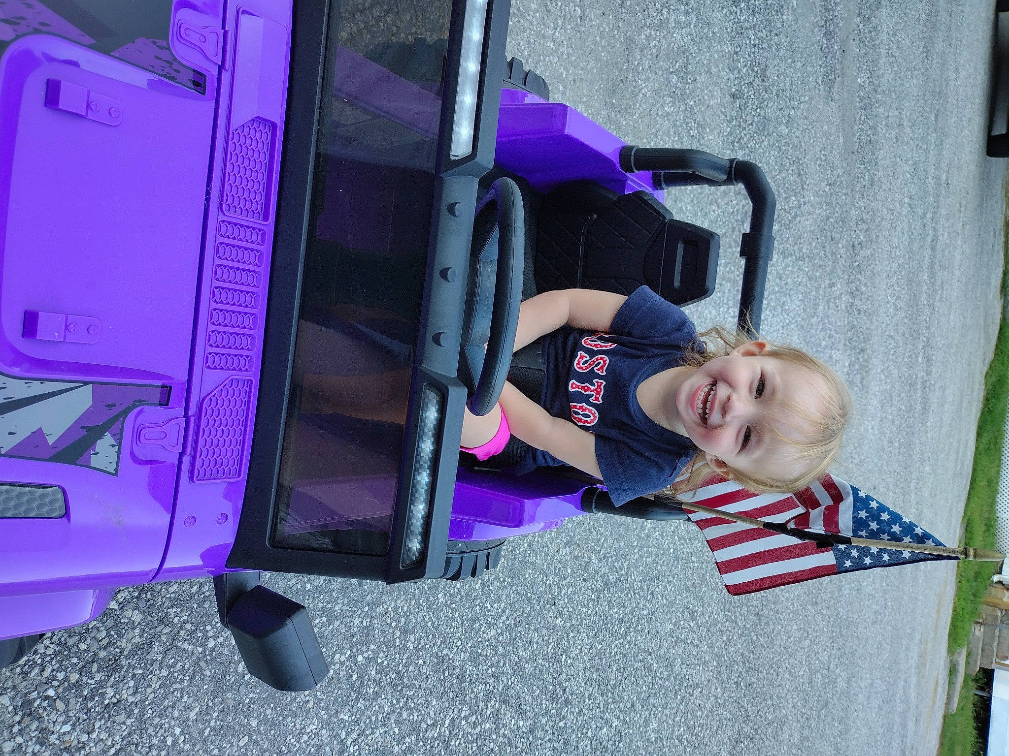 Lillyanna joined the competition — help win amazing prizes! automotive_exterior, bumper, child, electric_blue, flag, flag_of_the_united_states, fun, joy, leisure, machine, magenta, motor_vehicle, person, plant, purple, smile, t_shirt, tire, toddler, vehicle_door
