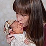 newborn, baby, woman, kiss, face, headband, bow, sleeping, tender, love, affection, portrait, closeup, skin, long_hair, clothing, hand, indoor, soft_background, family