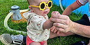 Aylah Mae joined the competition — help win amazing prizes! baby, child, sunglasses, yellow_sunglasses, grass, hand, adult_hand, sitting, outdoor, inflatable_pool, toy, shoe, person, shorts, hoodie, summer, playtime, sunny, fun, park