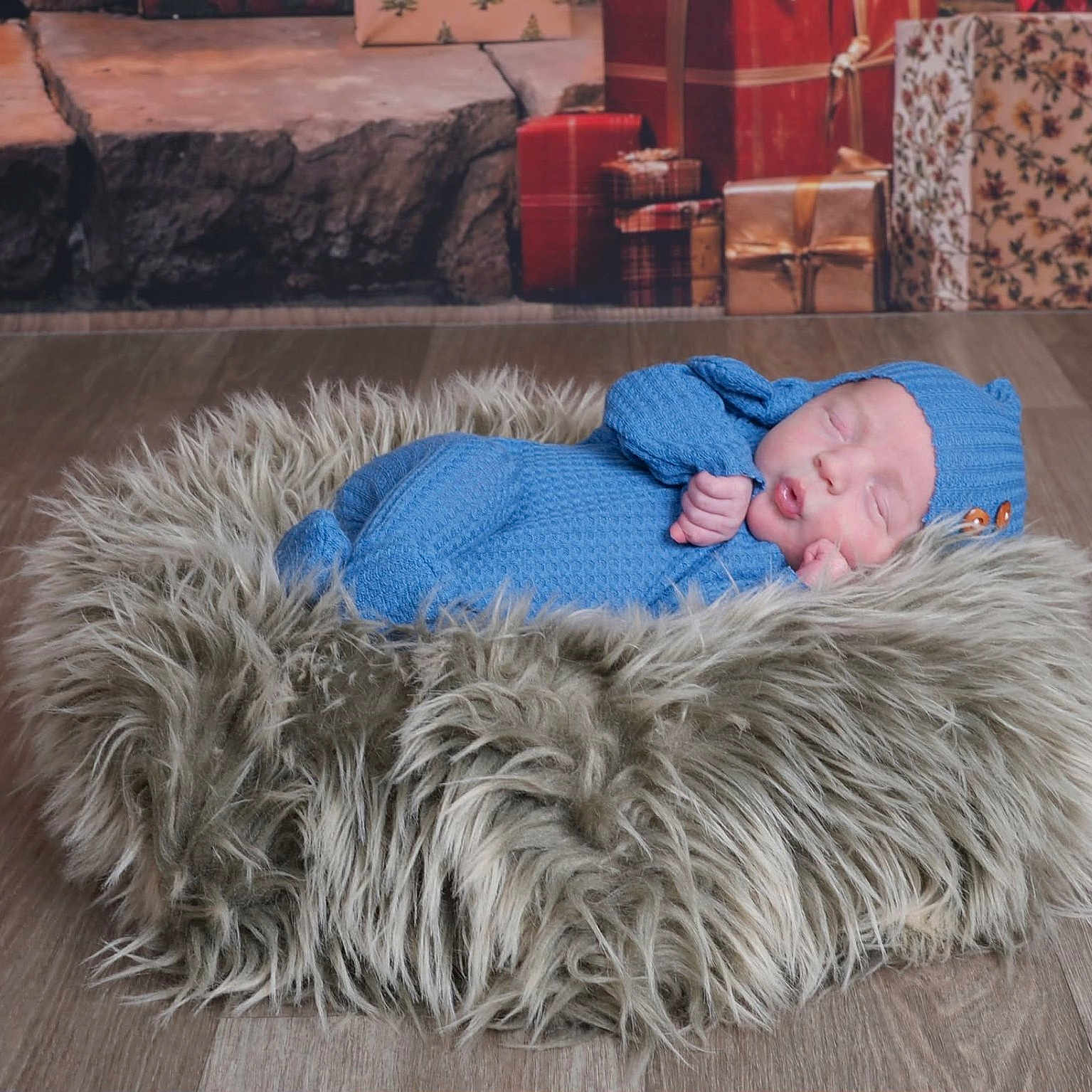 Draven is registered to the contest to win money with this photo: baby, newborn, sleeping, blue_outfit, knitted_clothing, fur_cushion, floor, wooden_floor, wrapped_presents, holiday_theme, cozy, peaceful, indoor, portrait, infant, cute, resting, warm, decor, soft_texture