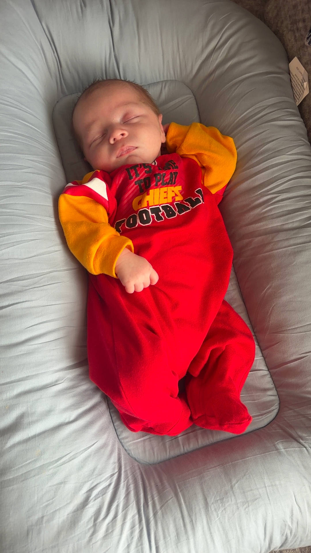 Colter joined the competition — help win amazing prizes! baby, child, cushion, cute, face, football, hand, head, indoor, infant, lounger, newborn, onesie, peaceful, person, red_clothing, resting, sleeping, soft_fabric, yellow_clothing