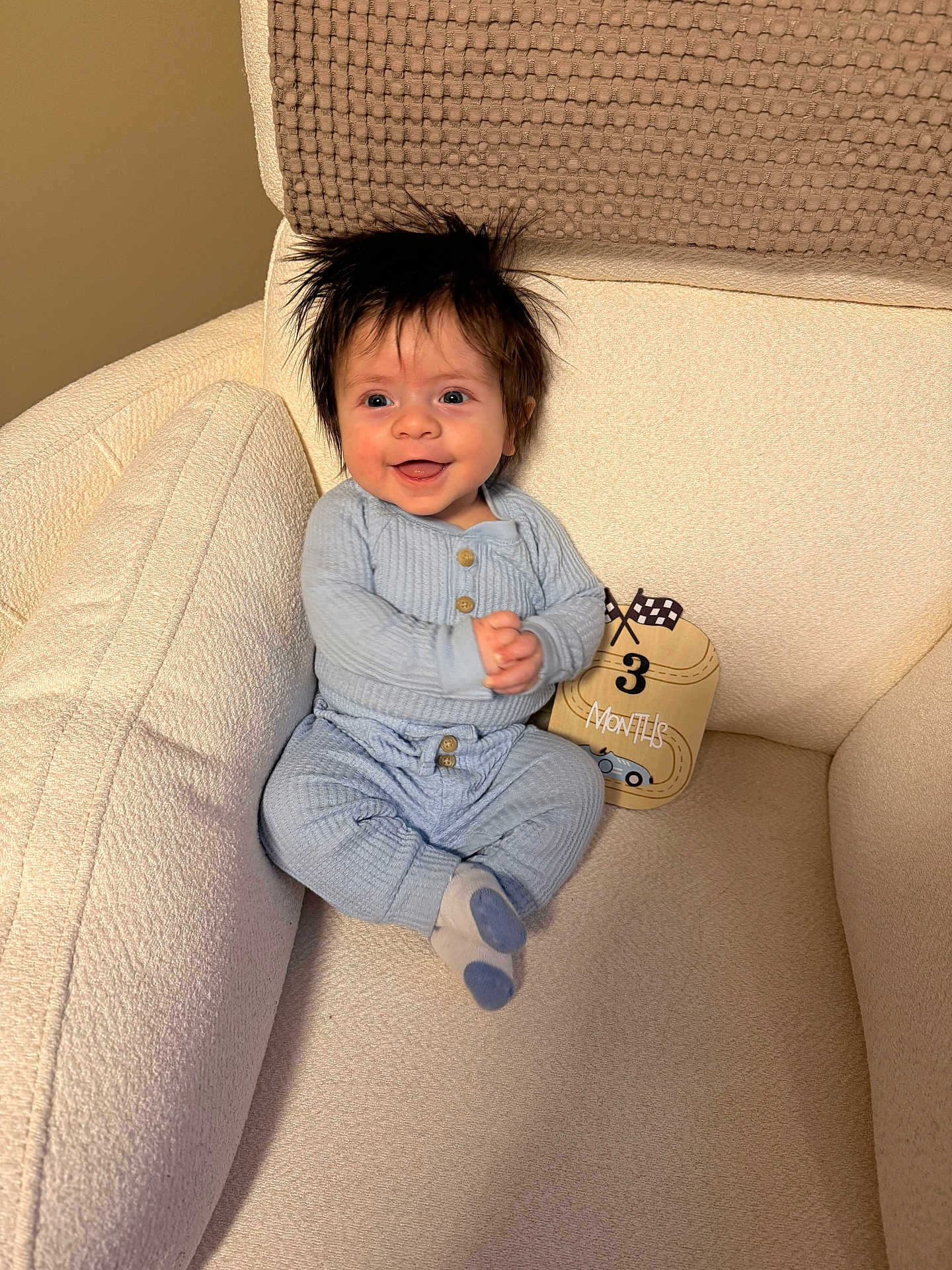 Bennett joined the competition — help win amazing prizes! baby, infant, smiling, spiky_hair, blue_onesie, socks, armchair, cushion, milestone_card, three_months, milestone, cozy, textured_fabric, portrait, happy, sitting, hands_clasped, indoor, nursery, soft_lighting