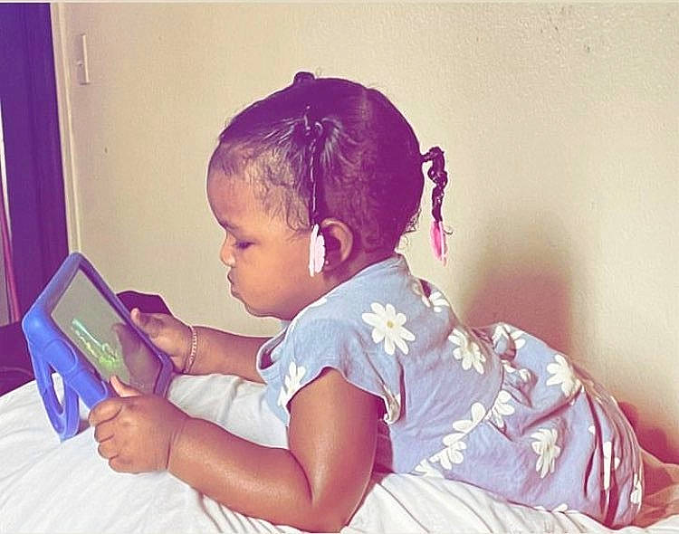 Skyler is registered to the contest to win money with this photo: baby_toddler_clothing, child, ear, eyelash, fashion_accessory, finger, fun, gadget, hair_accessory, hair_tie, happy, jewellery, magenta, person, pink, play, purple, room, sitting, tablet_computer