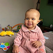 Aiyana is registered to the contest to win money with this photo: baby, child, smiling, pink_dress, indoor, toy, person, face, happy, sitting, lap, clothing, play, cute, infant, home, furniture, legwear, buttoned_dress, portrait