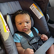 Uriel joined the competition — help win amazing prizes! baby, child, car_seat, safety_harness, curly_hair, blue_onesie, seatbelt, infant, car_interior, straps, serious_expression, cute, person, young_child, transportation, sitting, closeup, indoors, seat, human