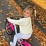 autumn, bicycle, bike, blonde_hair, child, cute, daylight, fall_leaves, girl, happy, nature, outdoor, park, patterned_pants, playful, road, smiling, sneakers, training_wheels, white_sweater