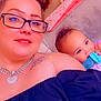 baby, blue_eyes, candid, casual, chewing, child, curly_hair, face, glasses, heart, indoor, jewelry, necklace, person, portrait, purple_clothing, smile, tattoo, toy, woman