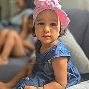 Ava a rejoint le concours — aidez-le/la à gagner de superbes lots ! blue_dress, blurred_background, bracelet, casual, child, couch, curly_hair, cute, expression, family, girl, home, indoor, person, pink_headwrap, portrait, sitting, soft_lighting, toddler, young_child