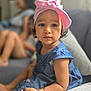 blue_dress, blurred_background, bracelet, casual, child, couch, curly_hair, cute, expression, family, girl, home, indoor, person, pink_headwrap, portrait, sitting, soft_lighting, toddler, young_child