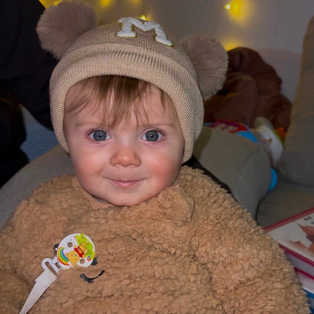 Maylone a rejoint le concours — aidez-le/la à gagner de superbes lots ! baby, beanie, blue_eyes, child, corduroy_pants, cute, face, fairy_lights, fuzzy_sweater, hat, indoors, infant, living_room, pacifier, pacifier_clip, portrait, smile, sofa, soft_texture, teddy_bear_ears