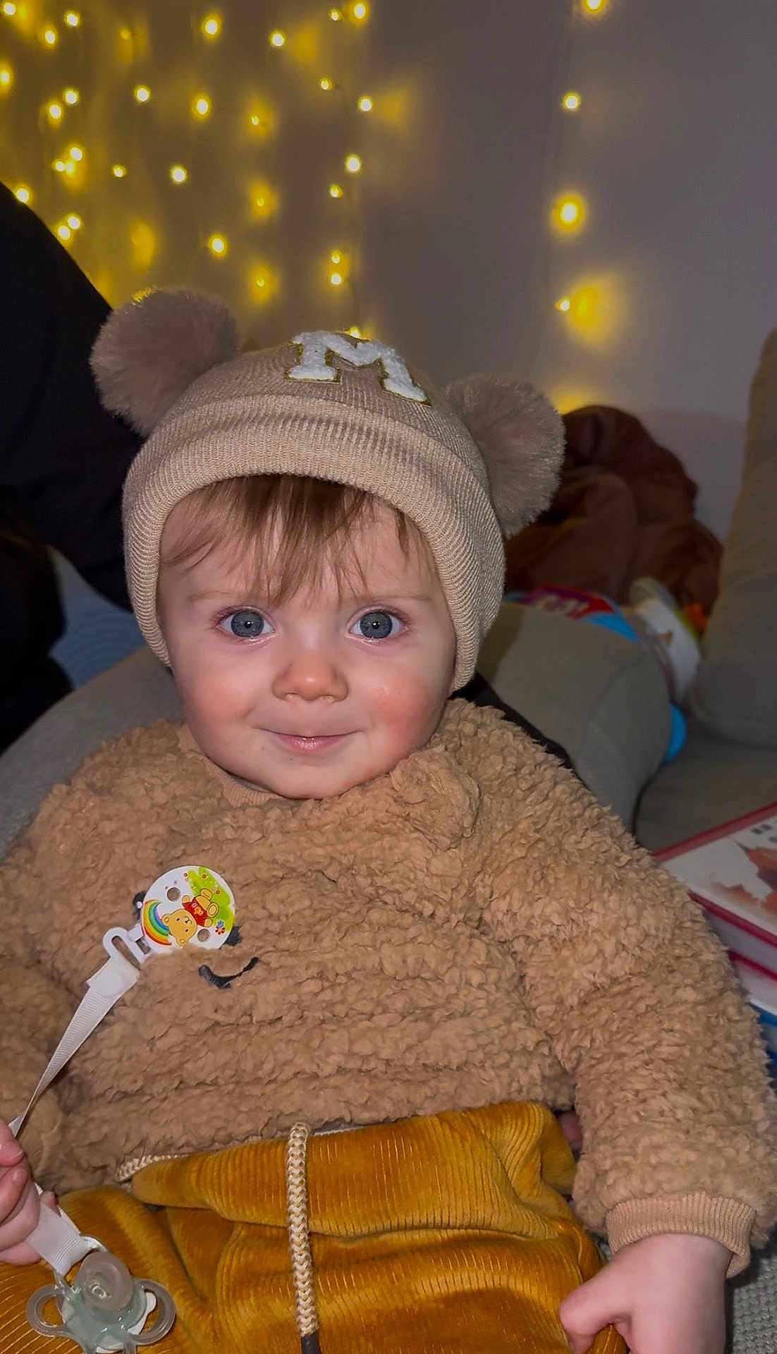 Maylone a rejoint le concours — aidez-le/la à gagner de superbes lots ! baby, child, infant, face, blue_eyes, beanie, hat, teddy_bear_ears, fuzzy_sweater, pacifier, pacifier_clip, corduroy_pants, living_room, fairy_lights, sofa, portrait, smile, cute, indoors, soft_texture