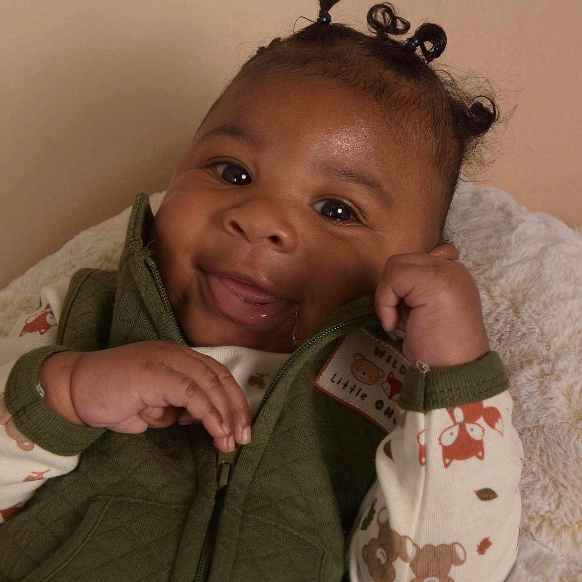 Kamere is registered to the contest to win money with this photo: baby, smile, face, hair_buns, green_vest, pajamas, bear_pattern, blanket, infant, cute, child, portrait, cozy, happy, indoors, person, closeup, soft_texture, warm_colors, expression