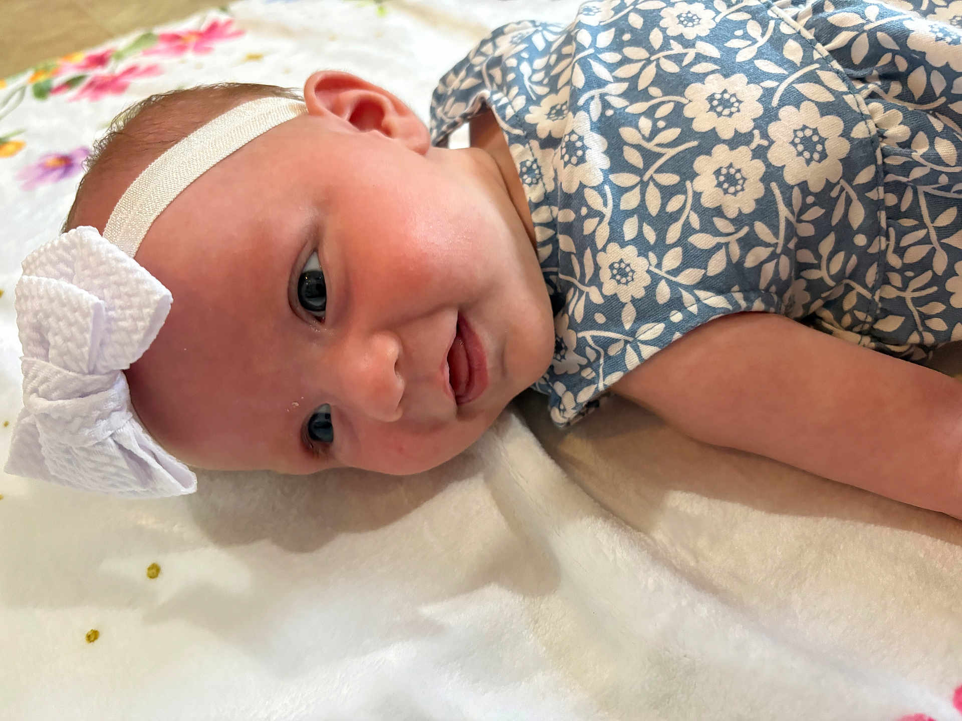 Maddelynn joined the competition — help win amazing prizes! baby, infant, headband, bow, blue_flower_pattern, blanket, smile, face, skin, cheek, eye, arm, lying_down, closeup, cute, child, soft, fabric, indoors, portrait