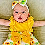 baby, infant, child, sunflower, headband, dress, yellow, cute, smile, face, arms, clothing, pattern, sitting, couch, indoors, happy, portrait, person, young