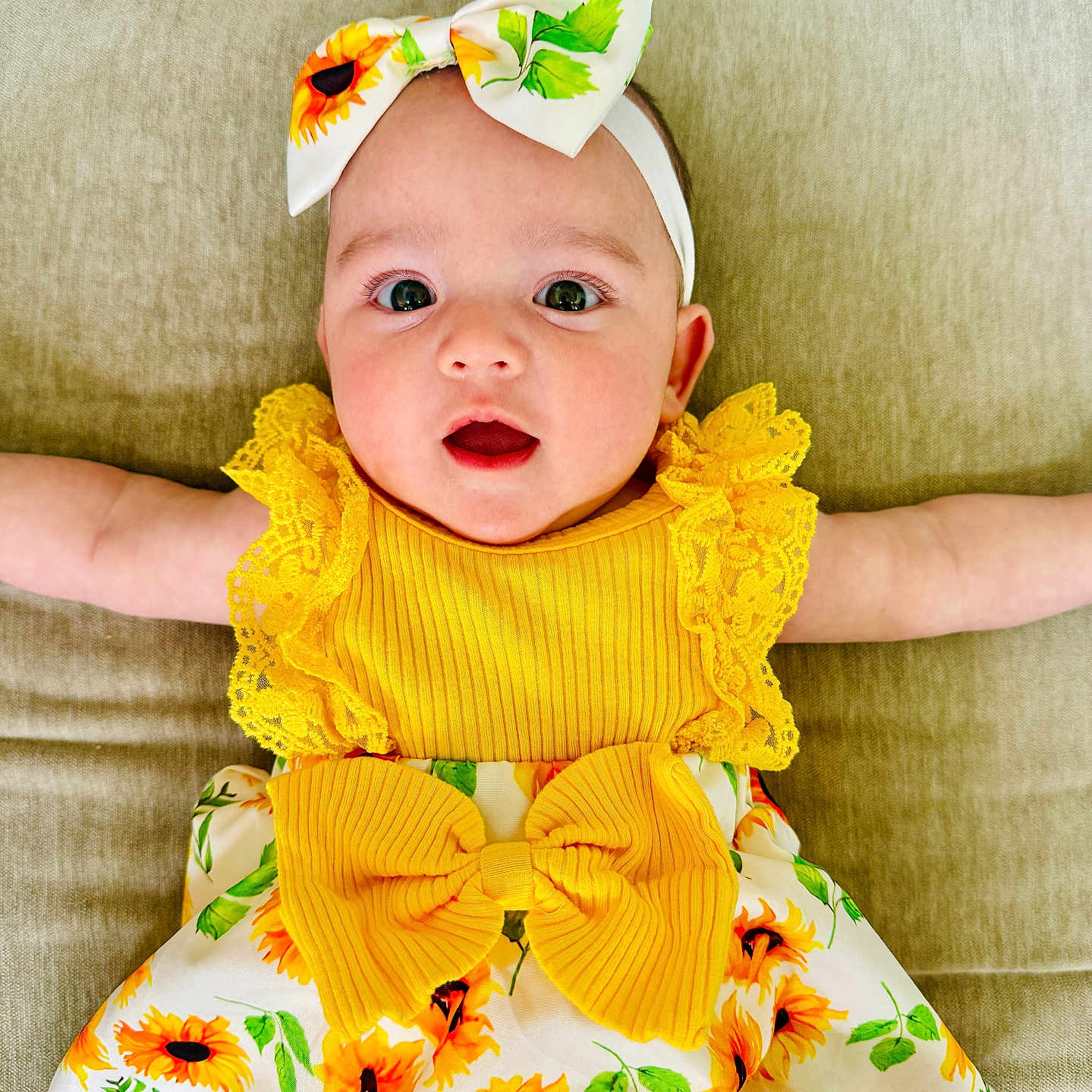 Arya Rosie joined the competition — help win amazing prizes! arms, baby, child, clothing, couch, cute, dress, face, happy, headband, indoors, infant, pattern, person, portrait, sitting, smile, sunflower, yellow, young